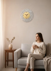Woman sitting on a couch holding a cup, with a decorative wall clock above her.